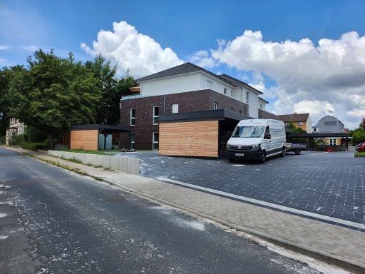 Moderne Wohnhäuser mit Holzverkleidung und grauem Pflaster vor einer ruhigen Straße.