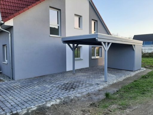 Helles Haus mit Carport und gepflasterter Auffahrt, umgeben von Rasenflächen.
