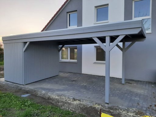 Carport aus Holz mit einem grauen Dach, angrenzend an ein Wohnhaus.