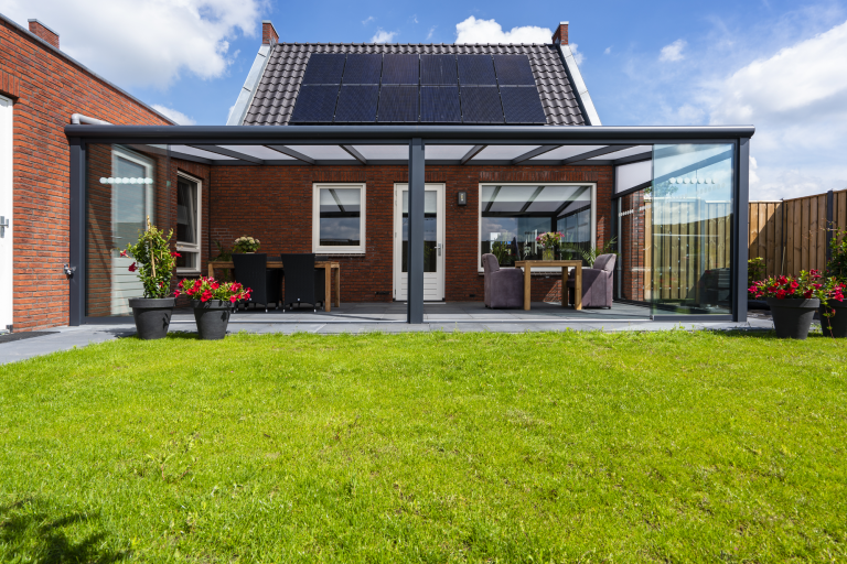 Modernes Haus mit Terrassenüberdachung und gepflegtem Rasen, umgeben von Pflanzen.