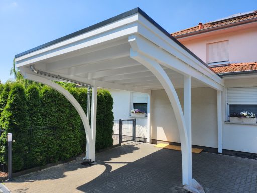 Carport mit weißen Säulen neben einem gepflegten Hecken und einem Wohnhaus im Hintergrund.
