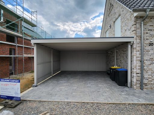 Offener Garagenraum mit grauem Boden und Mülltonnen neben einer steinernen Wand.